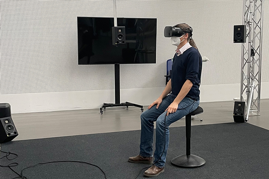 Proband mit VR Brille auf einem Hocker im Hörsimuator der TU Berlin
